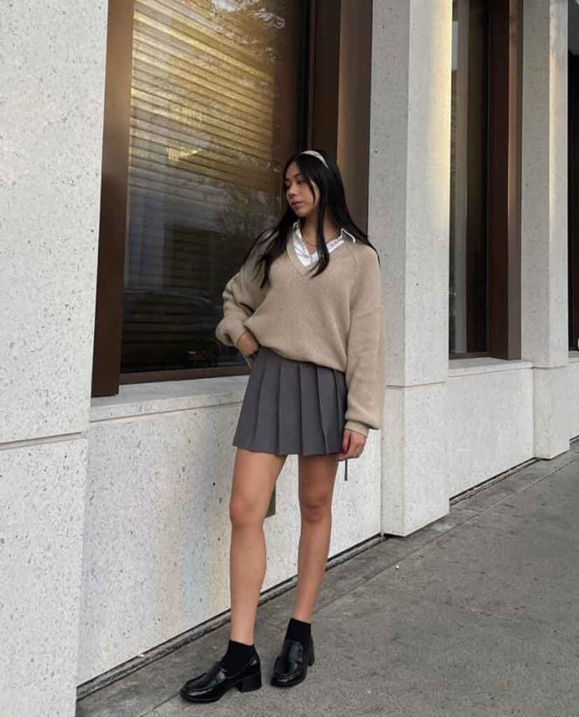 一位穿着毛衣和裙子的女性站在墙边 壁紙
