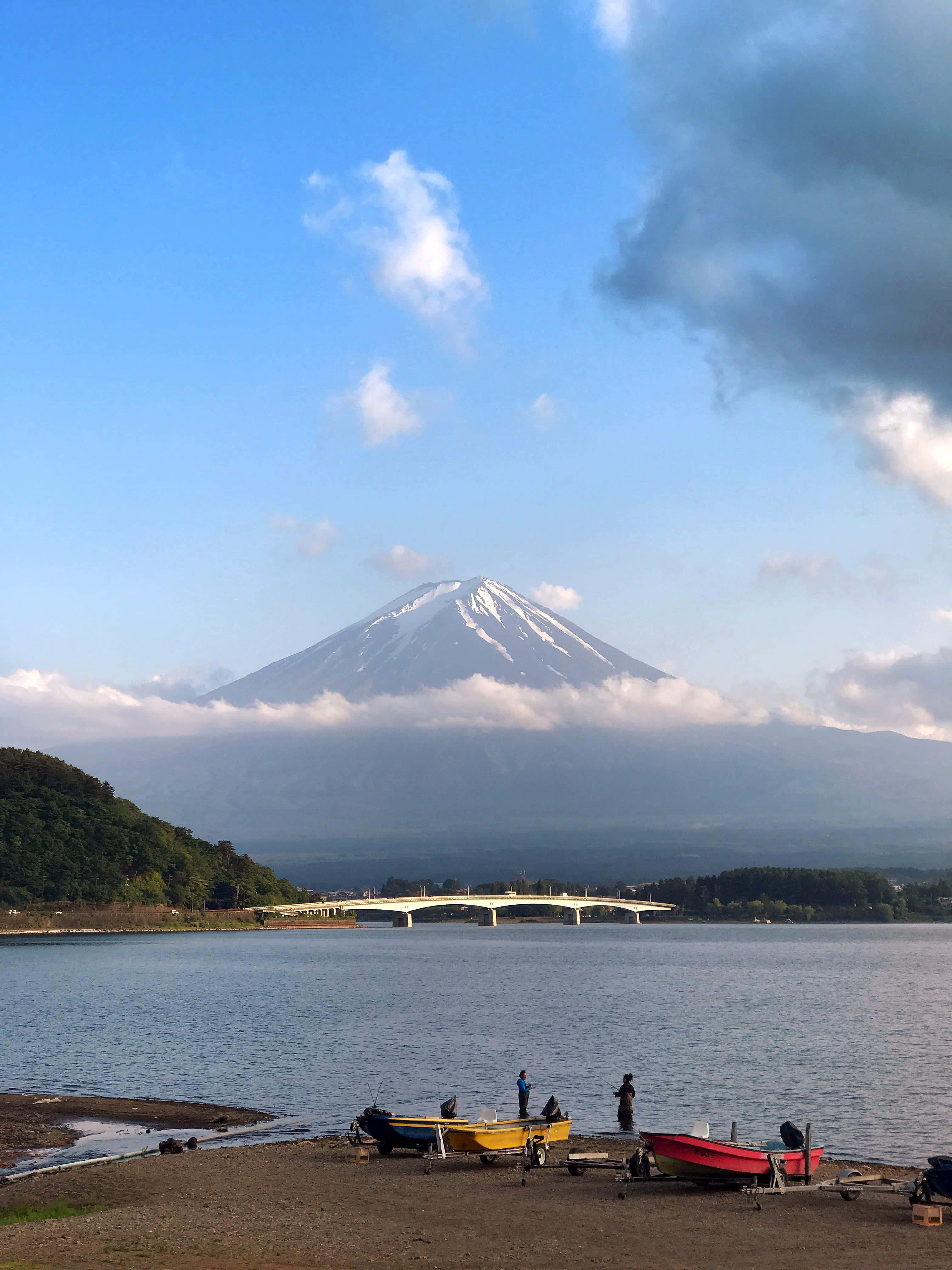 一群人坐在岸邊，背景有一座山 壁紙
