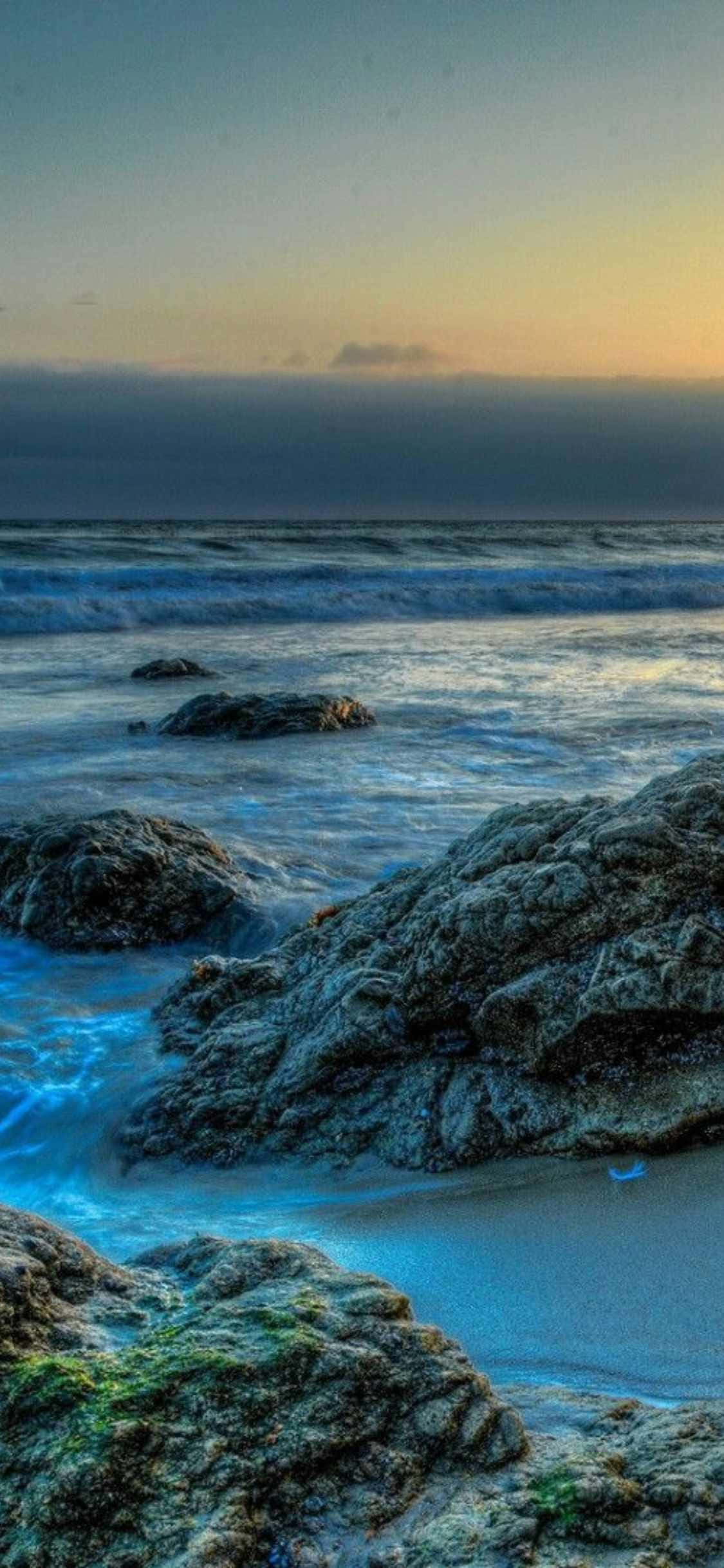 夕陽沙灘上的岩石與海水 壁紙