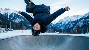 滑板少年在雪地山脉的半管上表演360度翻转。