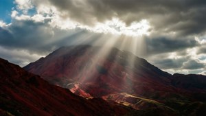 陽光穿透雲層照射在紅色山巒上，營造出戲劇性的光影效果