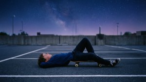 一位滑板少年在宁静的空地中，于星空下放松。
